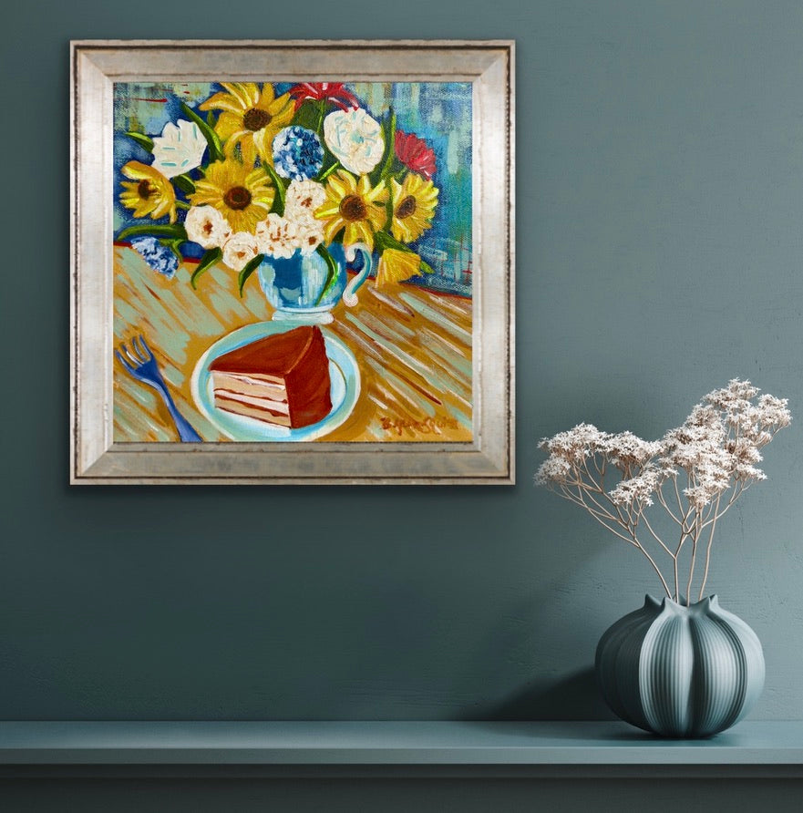 Framed painting of a still life with flowers and cake on a wall next to a vase with white flowers.
