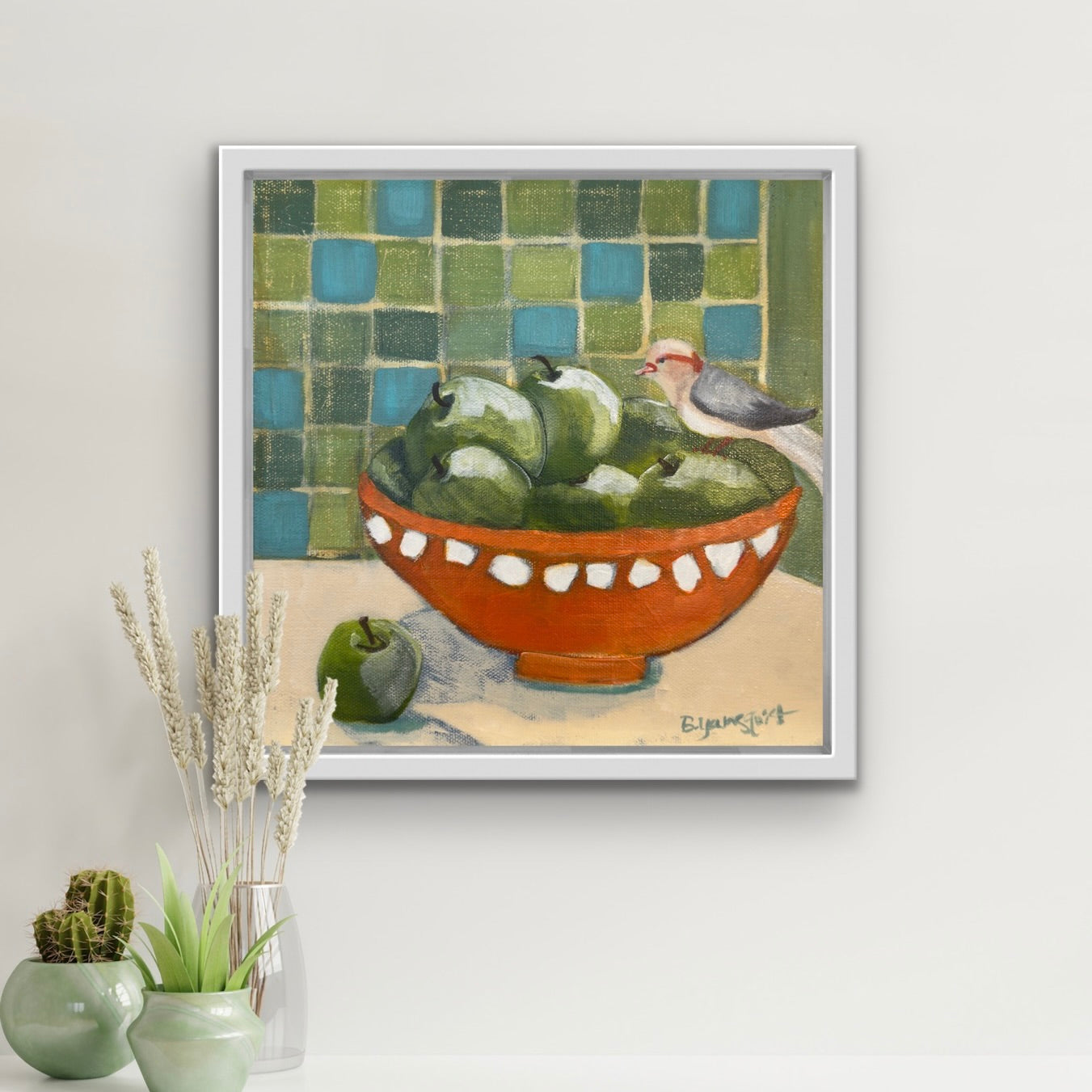 Framed artwork of a bird and apples on a tiled wall, with decorative plants below perfect for interior decor.l