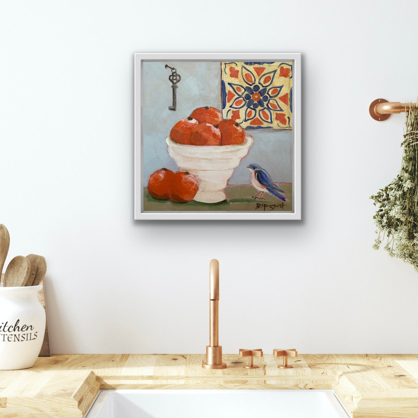 Framed original acrylic still life artwork above a kitchen sink with oranges and a bird on a white wall.