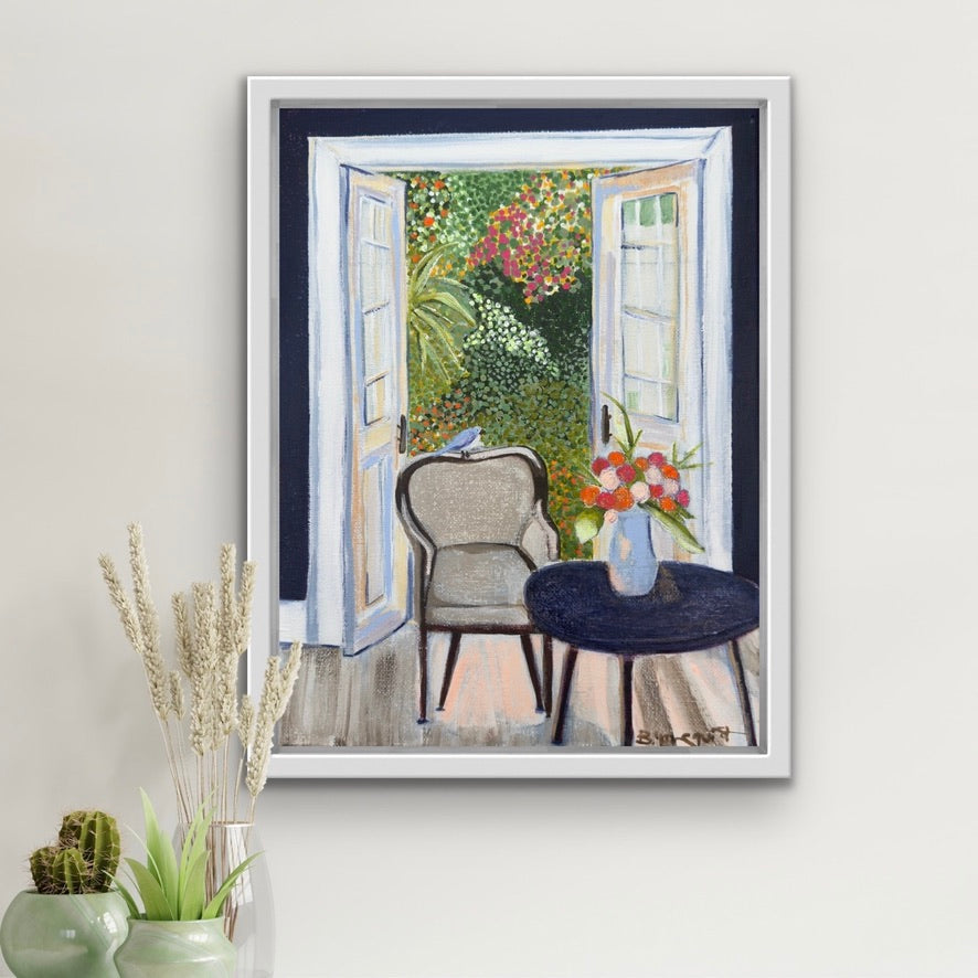 Framed artwork of a garden scene with a chair and table on a white wall for home decor