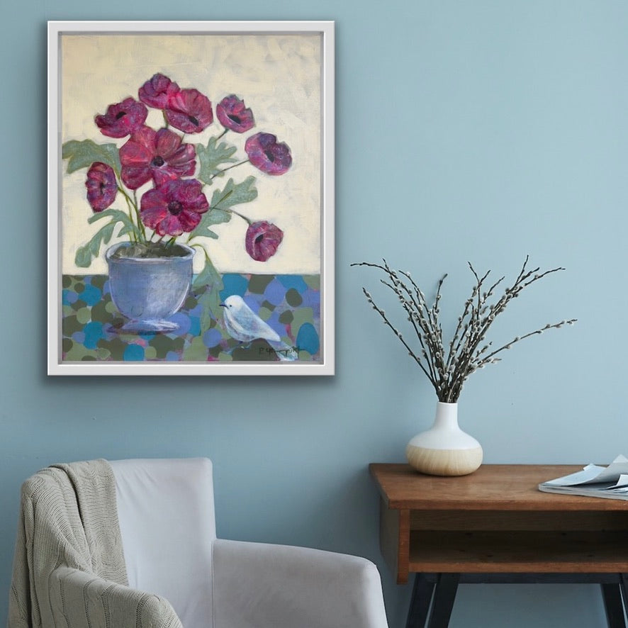 Framed floral painting for art collectors and home decor on a wall with a chair and table below.